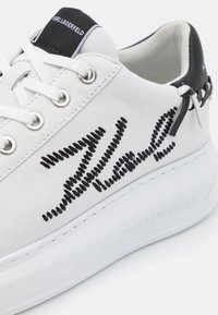Hvite lær sneakers med svart simulert sømdetalj, rund tå, flat hvit såle, og svarte detaljer på hælen og tungen.