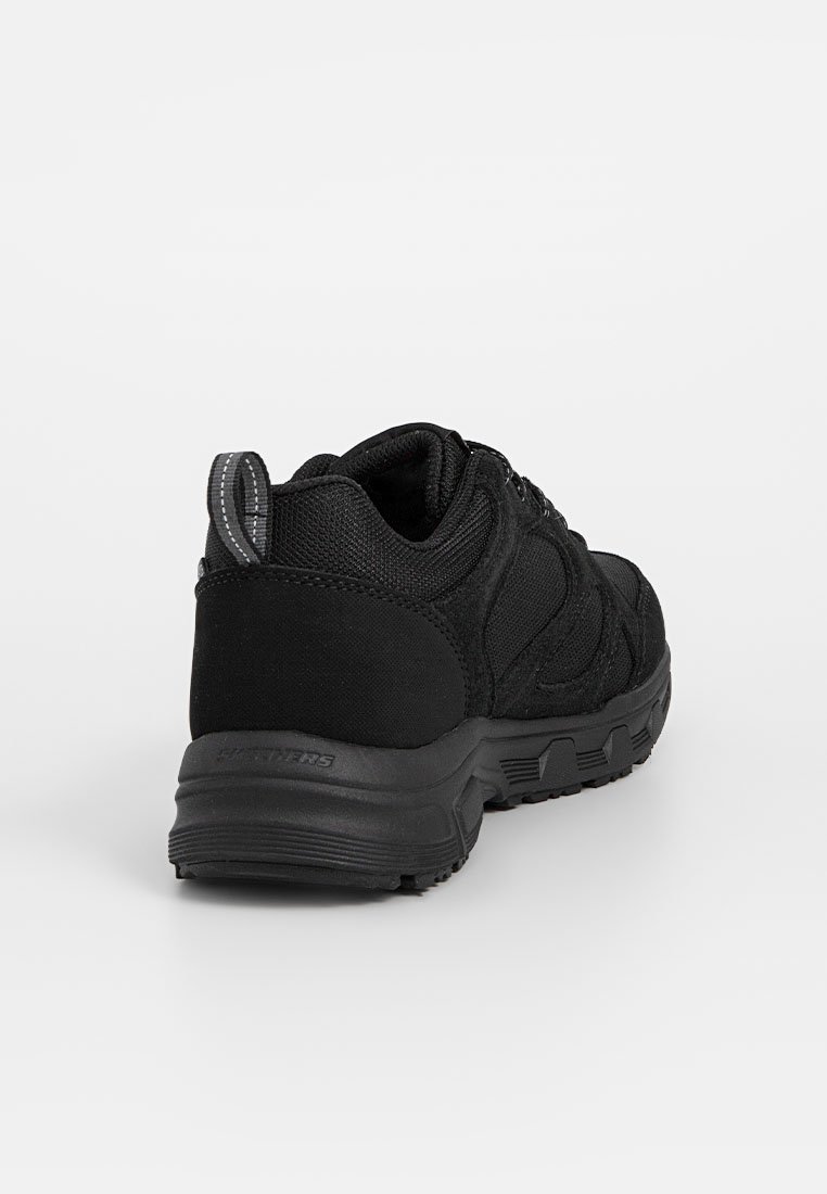 Zwarte sport sneaker met een gevoerde kraag, textuurzool, bovenwerk van mesh en stof, en een grijze trekstrop aan de hiel, weergegeven vanuit een achteraanzicht.