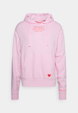 Sweat à capuche Adidas rose clair avec poche avant, cordons et texte sur la poitrine et la manche en rose plus foncé.