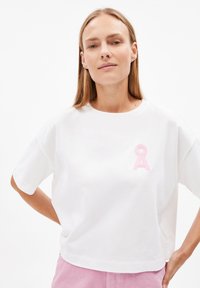 Witte katoenen t-shirt met een cropped ontwerp, voorzien van een lichtroze geborduurd lintdetail op de borst en korte mouwen.