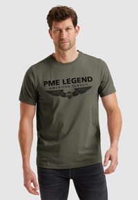 Olivově zelené tričko s krátkým rukávem s černým potiskem designu "PME LEGEND AMERICAN CLASSIC" a motivy křídel na hrudi.