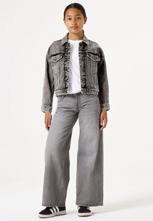Chaqueta de mezclilla gris con bolsillos frontales, cuello alto y bordes deshilachados. Combinada con jeans grises de pierna ancha y zapatillas negras con franjas blancas.