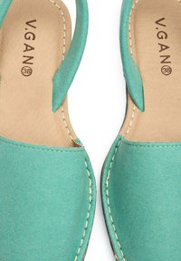 Turquoise vegan slip-on shoes with a soft texture, rounded shape, and beige stitched accents, labeled with "V.GAN" and size 38.