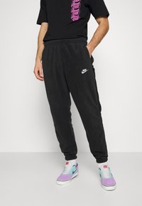 Svarta fleece-joggers med elastiska ärm- och midjeband, med en vit Nike-logotyp på vänster sida. Matchas med flerfärgade sneakers.