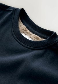 Mustapaita, jossa on pyöreä kaula-aukko ja pehmeä beige fleece-vuori. Kangas näyttää sileältä, ja kaulusreunassa on teksturoitu pinta.