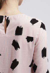 Blusa rosa con motivo a pennellate nere, tessuto leggero, chiusura con bottoni sul retro e scollatura arrotondata.