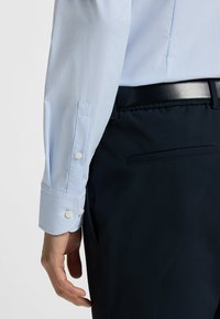 Ljusblå och vit randig skjorta med två-knapps manschetter, parat med mörkblå byxor med bakficka och texturerad väv.