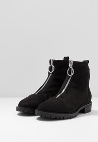 Bottines en daim noir avec fermetures éclair argentées et accents ronds. La semelle est texturée et épaisse, garantissant adhérence et stabilité.