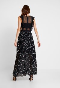 Černé maxi šaty s krajkovým živůtkem, zdobené volánovými krátkými rukávy a sukní s květinovým potiskem v růžových a zelených vzorech.