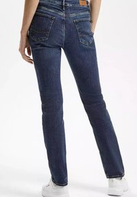 Wąskie dżinsy z ciemnoniebieskiego denimu z tylnymi kieszeniami i widocznym przeszyciem, charakteryzujące się średnim stanem i dopasowanym krojem do kostek.