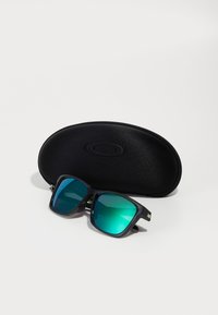 Gafas de sol rectangulares negras con lentes degradados en tonos teal, con un marco negro mate y un estuche duro negro protector con un logo.
