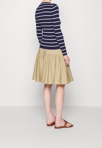 Gestreiftes navy-blaues und weißes Langarmshirt, kombiniert mit einem khakifarbenen Faltenrock. Braune flache Sandalen runden das Outfit ab.