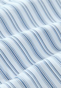 Baumwollstoff mit wellenförmigen blauen und weißen Streifen. Glatte Textur; die Streifen variieren in der Breite und bieten einen subtilen Must kontrast.