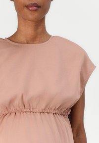 Light pink, short-sleeved top with a round neckline and gathered waistband. Soft fabric with a smooth texture and subtle draping.