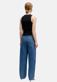 Hoge taille blauwe denim jeans met een losse fit, voorzien van twee achterzakken en een ruwe zoom, gedragen met een zwarte mouwloze top.