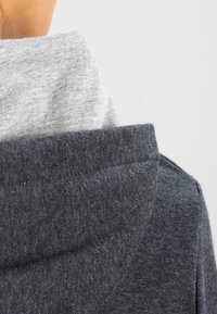 Hoodie met een grijze binnenvoering en een donkergrijze buitenstof. Zachte textuur, relaxte pasvorm en zichtbare stiksels op de kraag.