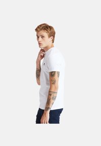 Weißes T-Shirt mit kurzen Ärmeln, das auf der Brust ein kleines Logo zeigt. Der Stoff wirkt weich und hat ein klassisches Rundhalsdesign.