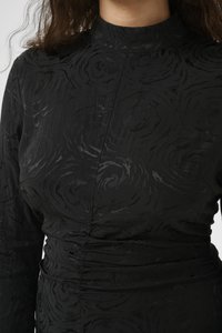 Black dress with a high neckline, featuring a textured floral pattern and gathered detailing at the waist. Smooth fabric with subtle sheen.