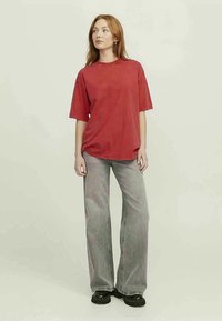 Červené oversized tričko s krátkým rukávem, kombinované se šedými pruhovanými širokými kalhotami. Model má na sobě černé platformové boty. Jednoduchý design, ležérní střih.