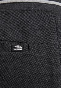 Tissu gris texturé avec un motif tissé, featuring une petite étiquette de logo noire Pull&Bear cousue sur une poche.