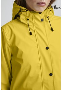 Yellow waterproof jacket with a high collar, adjustable drawstrings, black snap buttons, and smooth, glossy texture.