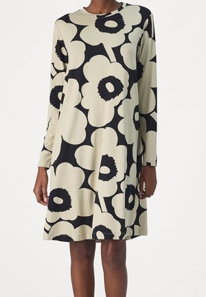 Robe à manches longues en tissu doux, avec un fond beige orné de grands motifs floraux noirs et des accents circulaires contrastants.