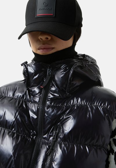 Czarna, błyszcząca kurtka puchowa z wysokim kołnierzem, zamkami z przodu i kapturem. Noszona na czarnym golfie, w komplecie z czarną czapką z logo.