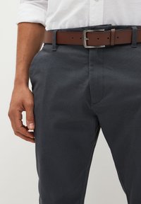 Pantaloni grigio scuro con trama, dal taglio slim, abbinati a una cintura in pelle marrone con fibbia in metallo argento. Focus su un design sofisticato.