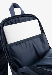 Interiér námorníckeho batohu s polstrovanou priehradkou na laptop, s hladkým textilným materiálom a zipsom na uzavretie. Popruhy sú textúrové a je viditeľná aj horná rukoväť.