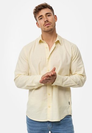 Lange mouwen, lichtgele blouse gemaakt van een gestructureerde stof, met een knoopsluiting aan de voorkant en manchetten, gecombineerd met lichtblauwe jeans.