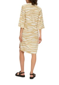 Beige Kurzarmkleid mit weißen Zebra-Streifen, das einen leicht geschwungenen Saum, seitliche Schlitze und ein lockeres Design aufweist.