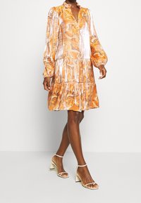 Orange marble-patterned dress with a collar, long puff sleeves, and tiered skirt. Worn with clear-strap block-heeled sandals.