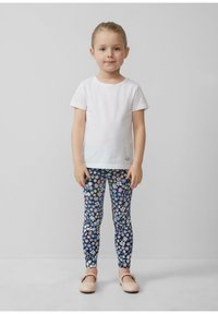 Weißes T-Shirt mit kurzen Ärmeln, leggings mit Blumenmuster in Blau, Pink und Gelb auf navy Hintergrund, und hellrosa flache Schuhe.