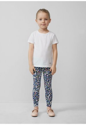 Weißes T-Shirt mit kurzen Ärmeln, leggings mit Blumenmuster in Blau, Pink und Gelb auf navy Hintergrund, und hellrosa flache Schuhe.