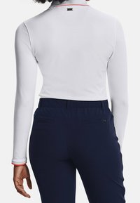 Haut blanc à manches longues avec un accent rouge autour du col, associé à un pantalon bleu marine à taille élastique avec deux poches arrière.