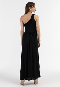 Rochie maxi neagră cu un umăr, fabricată dintr-un material ușor, având un talie strânsă și fustă fluida. Modelul poartă tocuri bej.