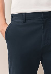 Pantalon bleu marine à texture lisse, doté de poches latérales et d'une fermeture par bouton à la ceinture. Conception à coupe ajustée.