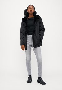 Sort polstret jakke med krave af kunstpels, lange ærmer og lynlås, parret med en ribbet sort top og grå skinny jeans. Svarte ankelstøvler.