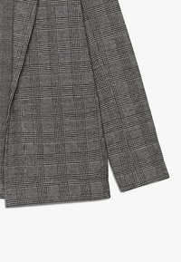 Blazer a quadri bianco e nero con una tessitura textured, caratterizzato da spalle strutturate, design a un bottone e rever a punta.