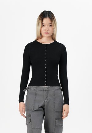 Black ribbed long-sleeve top featuring a round neckline and front button closure. Paired with gray cargo pants displaying multiple pockets.