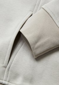 Ljust grå sweatshirtyta med en slät struktur, med ribbad mudd och fickdetalj. Enkel och minimalistisk design.