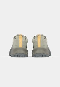 Trail shoes in muted green with a textured upper, reinforced heel, and yellow accent on the back. Rugged tread for grip on various surfaces.