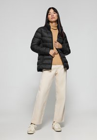 Giacca a vento nera, colletto alto, design trapuntato, abbinata a un dolcevita beige, pantaloni a palazzo crema e sneakers bianche.