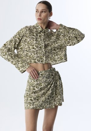 Ensemble de chemisier court et de jupe dans un motif de feuilles beige et vert, doté d'un tissu texturé et d'un design asymétrique.