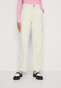 Beige cargobyxor med lös passform, två sidofickor, en knapp och bältesöglor. Bärs med svart och vit klumpig loafers.