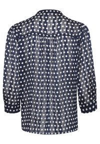 Blouse en voile bleu marine avec des pois blancs, manches longues, détail de pli au dos et manches à poignets, dotée d'un col classique.