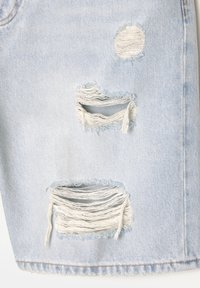 Denim azul claro con varias zonas desgastadas y deshilachadas. Roturas de diferentes tamaños, mostrando un aspecto casual y usado.