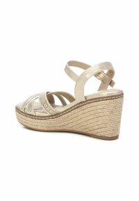 Sandalias de cuña en dorado metálico con plantilla de yute trenzado. Presentan un diseño de tiras entrecruzadas y una correa ajustable en el tobillo.
