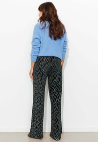 Pull bleu clair en maille douce, associé à un pantalon large noir à motifs zigzag pailletés. La tenue présente une silhouette décontractée.