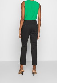 Czarne, dopasowane spodnie garniturowe o wąskim kroju, z gładką fakturą i dwoma tylnymi kieszeniami. Połączone z jaskrawozielonym, bezrękawnym topem.